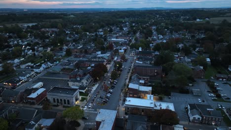 Aerial-view-of-a-small-town-at-dusk-with-cars-on-main-street-and-surrounding-houses