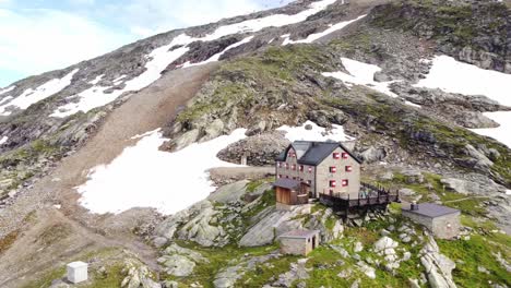 House-surrounded-by-stones-and-a-few-snow-field-with-a-rope-way-in-the-background-in-the-Alps-in-Kaernten,-Austria