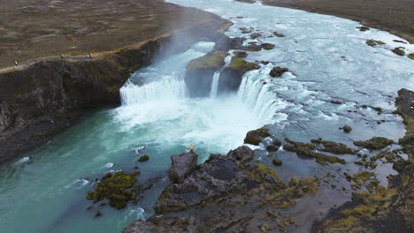 Turistas-Que-Visitan-La-Cascada-De-Godafoss-Con-Acantilados-Rocosos-En-Islandia