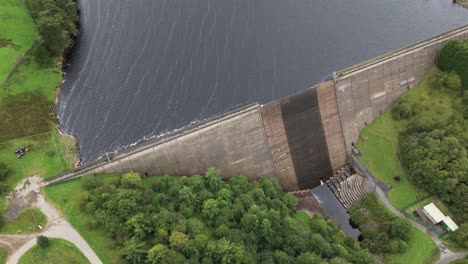 Booth-wood-reservoir-aerial-view-looking-down-circling-fresh-water-lake-and-concrete-dam-spillway,-West-Yorkshire