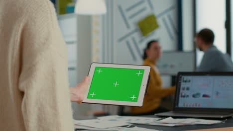 Woman-holding-tablet-with-green-screen-mockup-display-standing-in-busy-startup-business