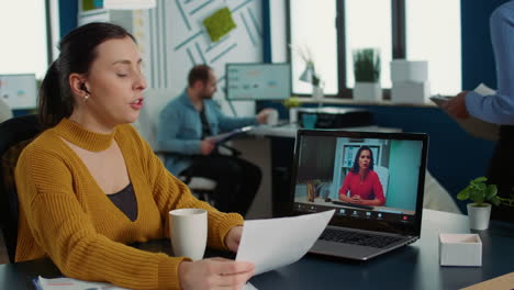 Portrait-of-startup-employee-presenting-paper-with-charts-using-laptop-in-casual-video-call-conference-with-manager