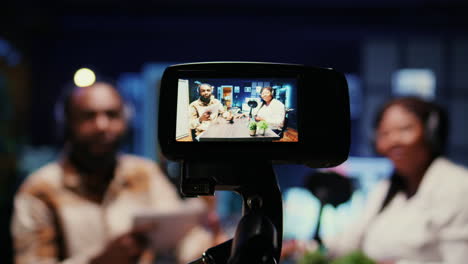 Focus-on-vlogging-camera-used-by-cohosts-in-blurry-background-streaming-podcast-during-live-debate