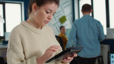 Portrait-of-woman-in-startup-office-picking-up-tablet-with-business-charts-and-interacting-with-touchscreen