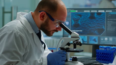 Male-scientist-looking-under-microscope-in-medical-development-laboratory