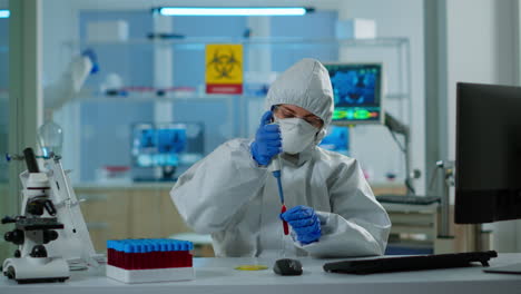 Science-technician-in-ppe-suit-using-micropipette-and-petri-dish-analysing-blood-sample