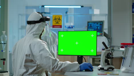 Scientist-man-wearing-protection-suit-typing-on-computer-with-green-mockup