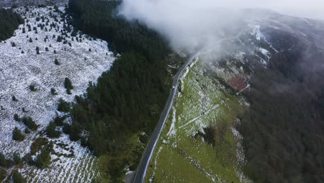 Reise-Durch-Wicklow:-Luftaufnahme-Eines-Weißen-Autos,-Das-Inmitten-Nebliger-Berge-Und-Schneebedeckter-Wälder-In-Die-Wolken-Fährt