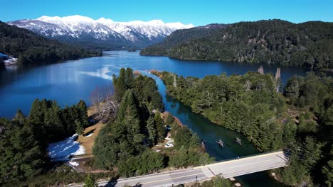 Highway-road-leading-over-forest-river-connecting-into-vast-lake,-aerial-view