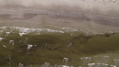 Ocean-waves-crash-onto-sandy-beach-with-high-tide-marks,-drone-top-down