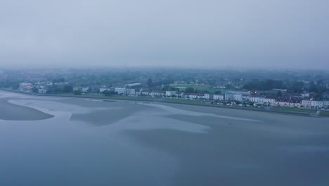 Mystical-Urban-Seaside:-Aerial-Fly-Around-of-Foggy-Sandymount-Beach-during-Low-Tide-on-a-Dark-Day-with-Cityscape-and-Beach-Walkers
