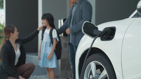 Progressive-family-with-EV-car-and-charging-station-prepare-daughter-to-school.