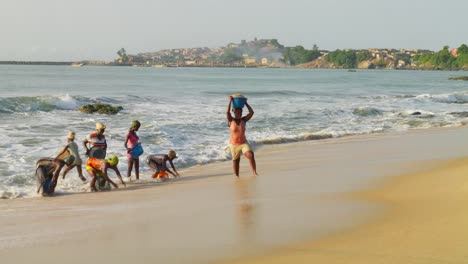 Afrikanische-Frauen-Sammeln-Und-Tragen-Sand-Am-Strand-In-Großen-Meereswellen