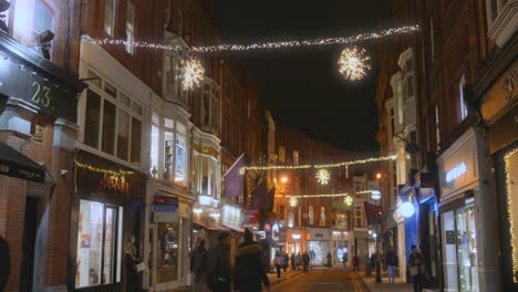 People-Walking-In-The-Shopping-Street-Decorated-By-Christmas-Lights-And-Ornaments-At-Night-In-Dublin,-Ireland