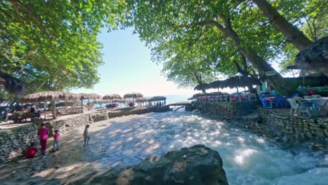 Restaurants-along-banks-of-San-Rafael-River-mouth-with-beach-and-sea-in-background,-Barahona-in-Dominican-Republic