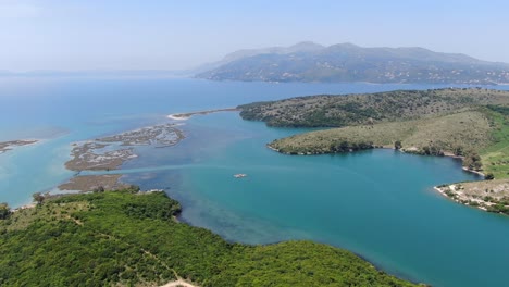 Drone-view-in-Albania-flying-over-wide-river-and-green-landscape-next-to-the-sea-with-mountains-on-the-back