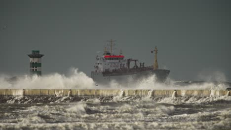 Storm-waves-crash-over-cement-IJmuiden-pier-with-ship-in-background,-telephoto