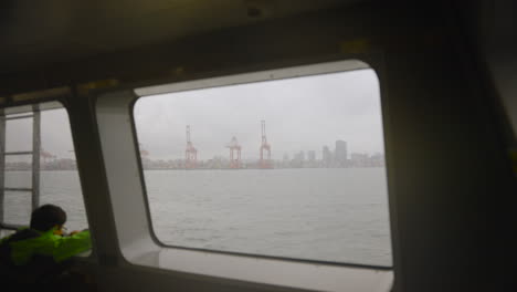 A-young-adventurer,-gazing-through-a-rainy-window-on-the-Vancouver-Sea-Bus,-captivated-by-the-towering-cranes-on-the-distant-horizon