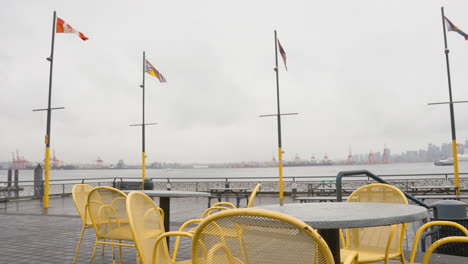 A-left-to-right-dolly-shot-of-empty-yellow-chairs-on-a-pier-against-Vancouver's-city-skyline,-with-the-SeaBus-and-various-flags-visible