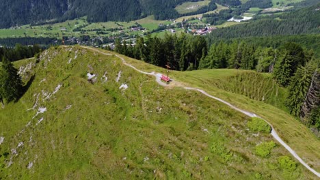 Rote-Bank-Steht-Auf-Dem-Gipfel-Eines-Kleinen-Berges,-Der-Mit-Grünem-Gras-Bedeckt-Ist-Und-Neben-Einem-Tal-In-Den-Alpen-In-Tirol,-Österreich