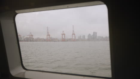 Peering-through-a-rain-kissed-window-aboard-the-Vancouver-Sea-Bus,-catching-sight-of-cranes-standing-tall-against-the-horizon
