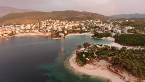 Drone-view-in-Albania-flying-over-blue-crystal-clear-water-on-sunset-and-hotels-with-red-light-in-Ksamil