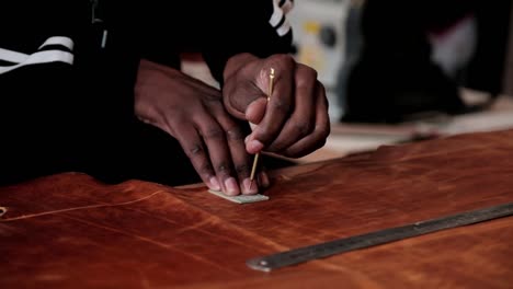 A-man-uses-a-stencil-to-cut-out-shapes-from-a-large-piece-of-leather-to-make-leather-goods