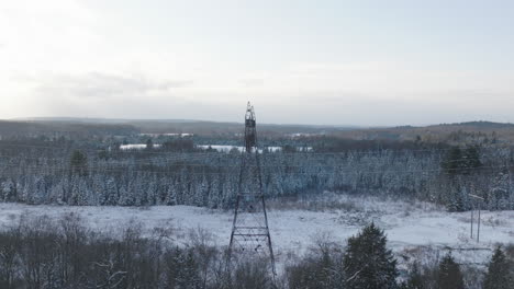 High-Voltage-Electrical-Tower-in-a-Snowy-Winter-Forest,-Aerial