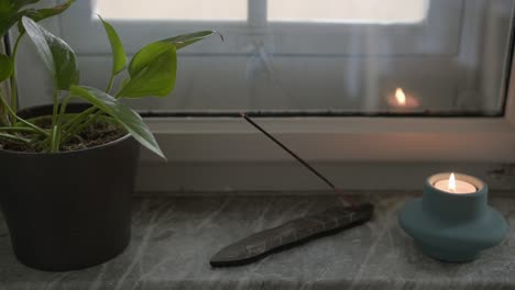 Smoke-form-incense-stick-and-relaxing-candle-next-to-living-room-window,-yoga-and-meditation-ritual