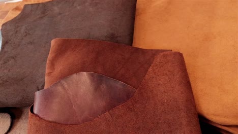 Three-different-rich-brown-and-caramel-colours-of-leather-laying-on-a-work-bench-ready-to-be-processed-into-leather-goods-by-a-small-artisan-business