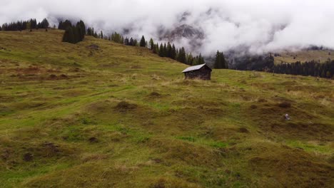 Low-aerial-shot-flying-on-grass-mountain-towards-small-wooden-hut-in-Austria