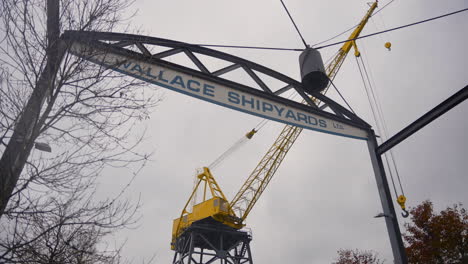 A-gentle-left-to-right-dolly-movement-of-the-Wallace-Shipyards-sign,-a-vibrant-yellow-crane-in-the-backdrop