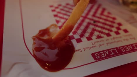 Close-up-shot-of-hands-dipping-a-fries-in-Ketchup-on-the-paper-and-taking-away-the-fries