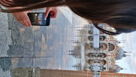 Young-traveler-woman-taking-reflection-pictures-of-Basilica-di-San-Marco-during-Acqua-Alta-period,-vertical