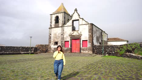 Woman-walks-leaving-behind-old-church-ruins-in-São-Mateus-da-Calheta,-Azores