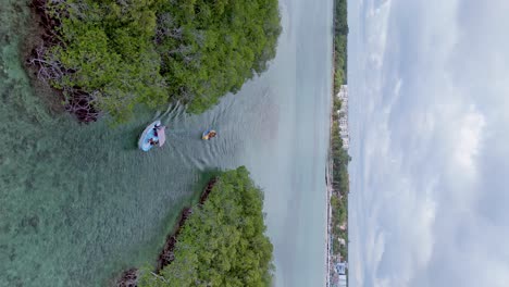 Vertikale-Drohnenaufnahme-Eines-Schnellboots,-Das-Ein-Bananenboot-Zieht,-Mit-Touristen,-Die-Sich-An-Einem-Bewölkten-Tag-In-Der-Bucht-Von-Santo-Domingo-Vergnügen