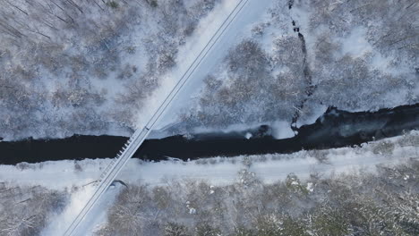 Puente-De-Invierno-Cruzando-Un-Río-Parcialmente-Congelado,-Antena-Arriba-Hacia-Abajo