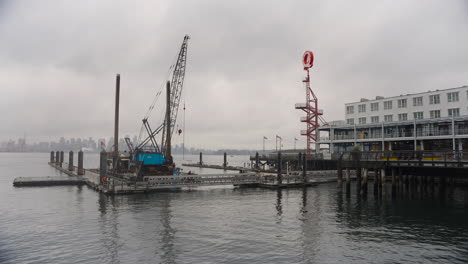A-commercial-sized-boat,-equipped-with-a-crane,-is-docked-in-a-harbor,-with-a-hotel-and-sign-visible-in-the-background