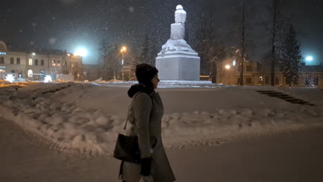 Beautiful-woman-in-winter-attire-walks-on-lonely-street-in-snowfall-at-night