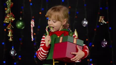 Kid-girl-in-Christmas-elf-Santa-Claus-helper-costume-licking-candy-cane-lollipop-caramel-sweets