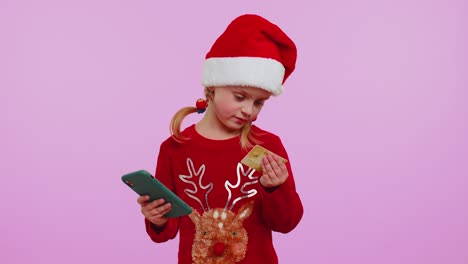 Mädchen-Im-Weihnachtspullover-Benutzt-Smartphone-Mit-Kreditkarte,-Während-Sie-Geld-Beim-Online-Einkauf-überweist