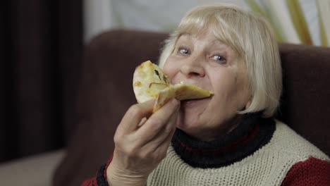 Beautiful-elderly-woman-is-sitting-on-sofa-and-eats-pizza