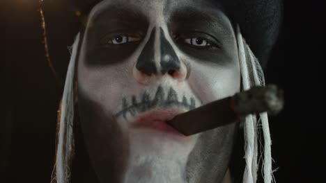 Close-up-shot-of-creepy-man-face-with-skeleton-makeup-smoking-cigar,-making-faces,-looking-at-camera