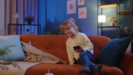 Child-toddler-hold-smartphone-watching-funny-cartoons,-chatting-with-friends-on-couch-alone-at-home