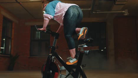 Athletic-girl-make-acrobatic-trick-on-bike-exercising-workout-on-stationary-cycling-machine-indoors