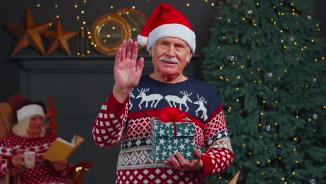 Senior-grandfather-in-Christmas-sweater-smiling-friendly-at-camera-and-waving-hands-gesturing-hello