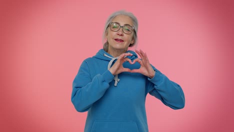 Smiling-senior-woman-makes-heart-gesture-demonstrates-love-sign-expresses-good-feelings-and-sympathy