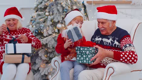 Enkelin-Tauscht-Weihnachtsgeschenk-Geschenkboxen-Mit-Erstauntem,-Glücklichem-älteren-Großvater-Zu-Hause-Aus