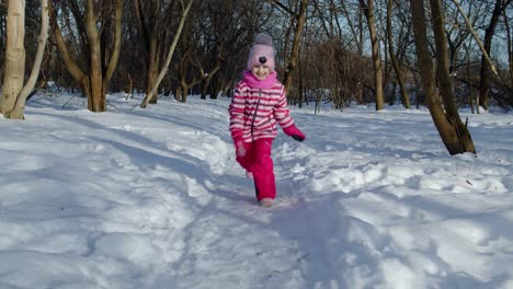 Joyful-little-child-girl-running-towards-on-snowy-road,-looking-at-camera-in-winter-park-forest
