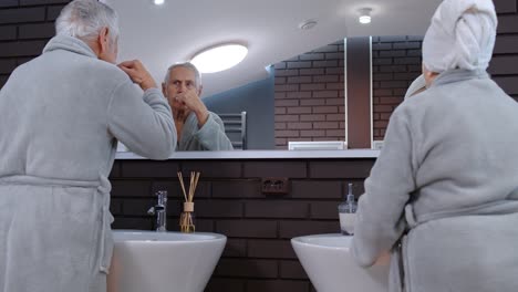 Senior-couple-grandmother-and-grandfather-brushing-teeth-and-looking-into-a-mirror-at-bathroom